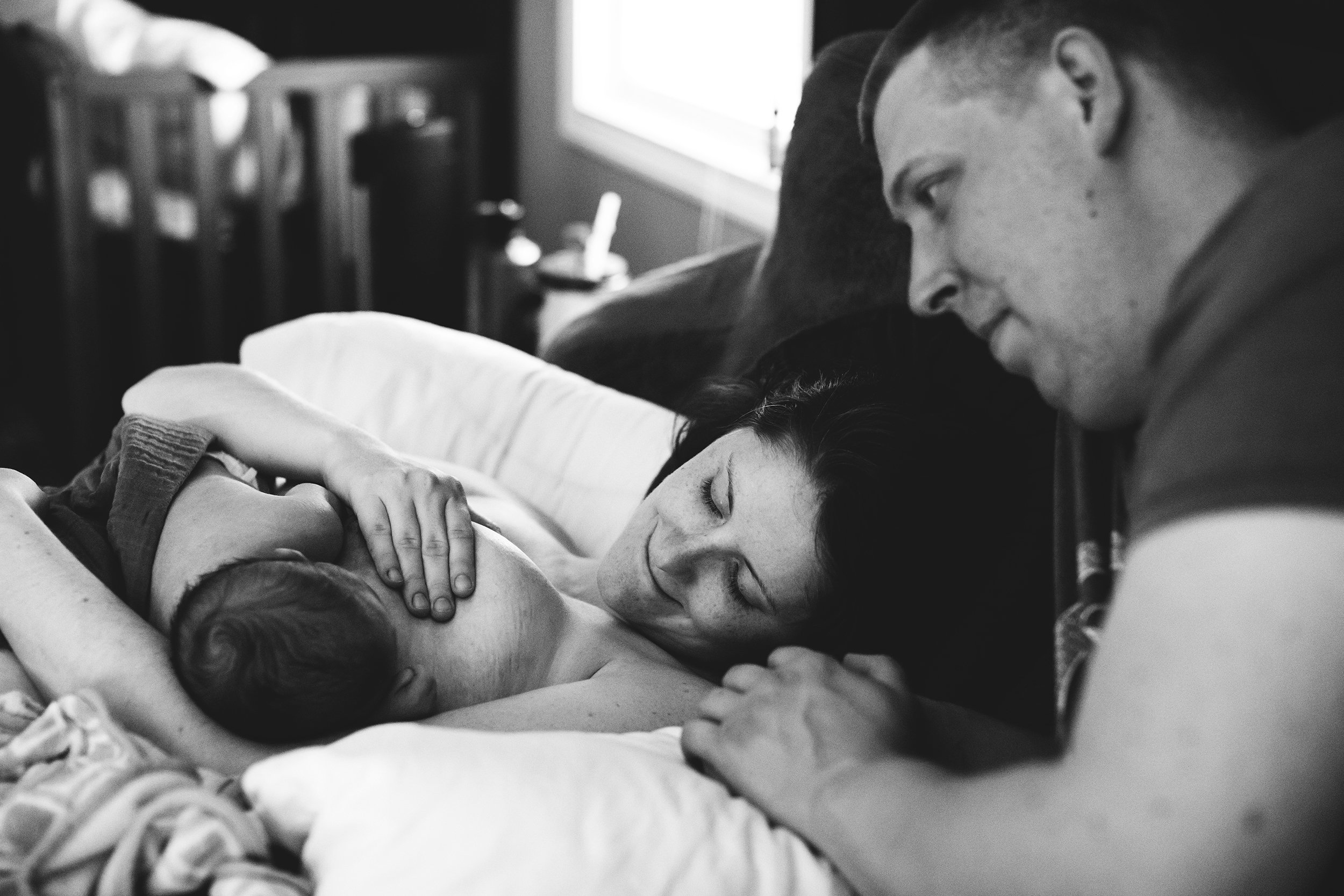new mom nursing breastfeeding newborn baby as dad watches after a home birth